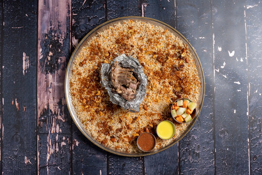 Flat lay of mutton madfoon mandi with vegetables and sauces