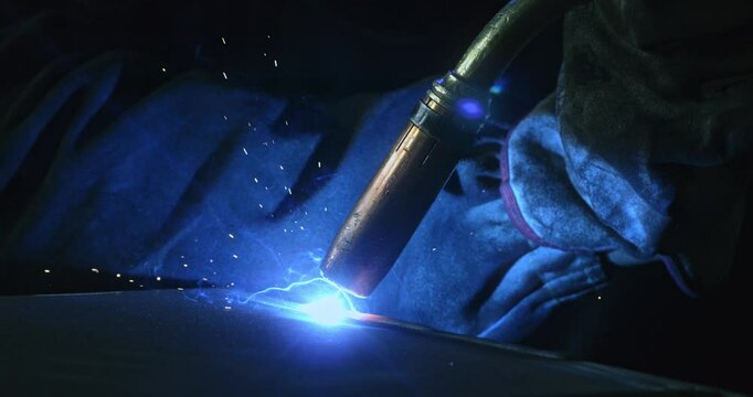 Super slow motion macro of welder blacksmith is welding metal steel with industrial tool with flying sparks in workshop at 1000 fps.