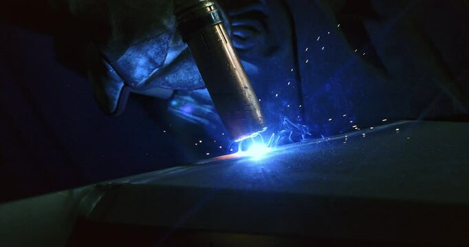 Super slow motion close up of welder blacksmith is welding metal steel with industrial tool with flying sparks in workshop at 1000 fps.