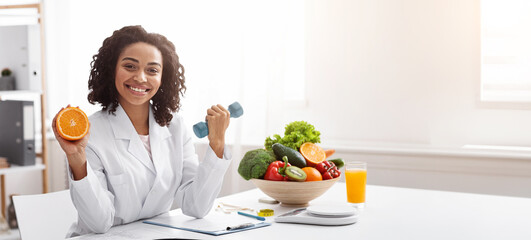 Sport and vitamins for immunity. Happy black woman doctor holding orange and barbell in clinic,...