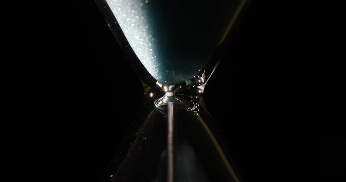 Glittering sand falls down through antique hourglass on black background. Old measuring instrument shows time run out. Concept of life passing