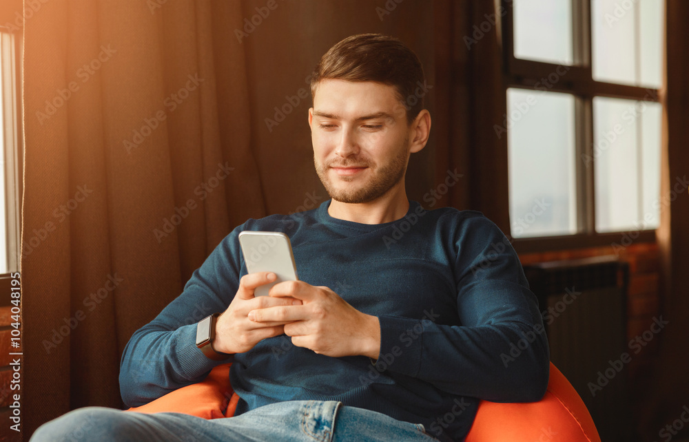 Aufkleber mobile app. student guy using phone texting and browsing internet sitting in beanbag chair indoor. s