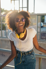 Happy young woman wearing headphones and sunglasses is laughing outdoors