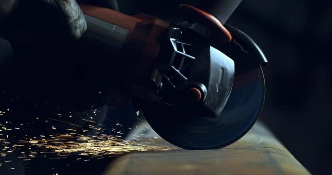 Super slow motion macro of blacksmith welder is working metal steel with industrial angle grinder with flying sparks in workshop at 1000 fps.
