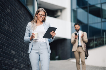 Businesswoman walking and using tablet outside office building