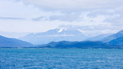 Snow-capped mountains rise from the foggy shores of Resurrection Bay in Seward, Alaska, where sea and sky blend in a hauntingly beautiful coastal wilderness.