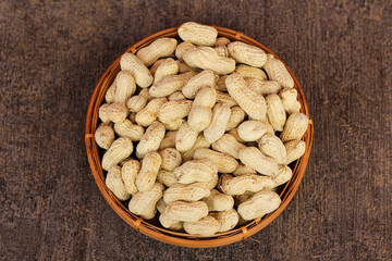 Unpeeled peanuts in a container isolated on a dark background. close up of salted shell peanuts.