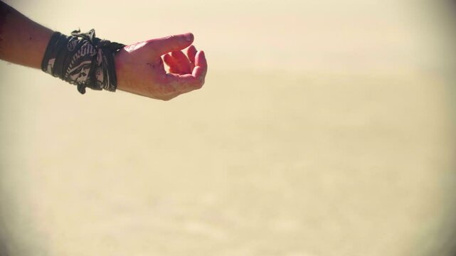 Close-up of blood covered and wristband-clad male hand reaching out to grab a flowing black cloth. A man captures elusive person in the desert by their flowing clothes.
