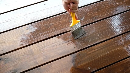 Close-up of a brush painting wood floor in brown color. Wood plank impregnation. Finish oil coating of board. Second layer of oiling. Manual construction work in a gazebo. Natural building materials