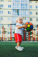 A one-year-old boy in a white T-shirt plays with a ball. TODDLER plays soccer. child development after one year