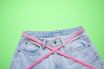 Jeans and measuring tape on green background, top view