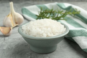 Sea salt in bowl on gray textured table, closeup
