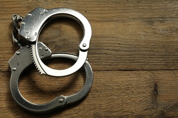 Classic chain handcuffs on wooden table, top view. Space for text