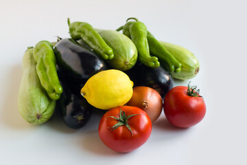 Group of fresh vegetables, eggplant, tomato, lemon and green pepper on white surface
