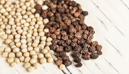 Black and white peppercorns on a white wooden table.