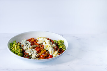 Large bowl of chefs salad with cheese, eggs, peppers, bacon on lettuce
