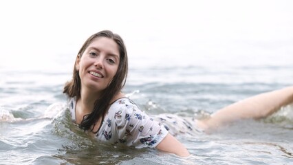 Fototapeta premium Calm woman in wet dress lies on shallows in river and touches water