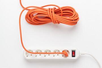 Flat lay photo of European 5-way power strip earthed on white background with long orange cord connected. Not isolated.