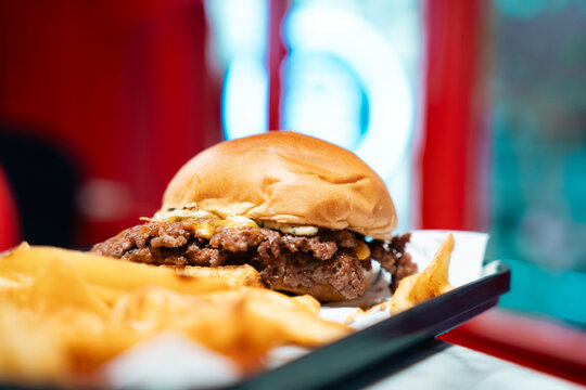 A delicious smashed burger served with fries on a tray. The background features blurred bokeh lights, creating a relaxed dining atmosphere.