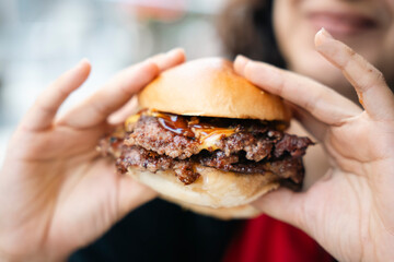 Close-up of a hand holding a burger with melted cheese and barbecue sauce. A relaxed dining...