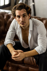 Portrait of a handsome young stylish sexy man in a white shirt, jeans jacket posing in studio with a loft interior. Black and white. Casual clothes, modern style