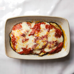Delicious baked eggplant dish topped with marinara sauce and melted cheese, served in a textured white baking dish.