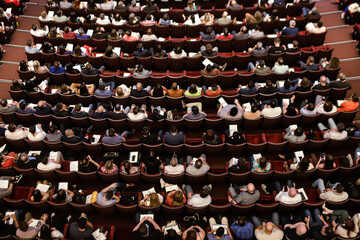 Theater audience with a view from above with almost all the seats occupied, arranged in rows.