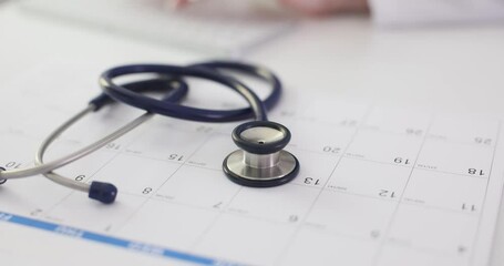 Doctor marks appointment date on calendar in medical office. Stethoscope lies on surface capturing moment of organization in medical setting