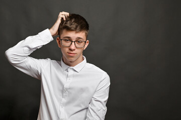 A doubting boy, thinking, scratching his head. on a gray background.