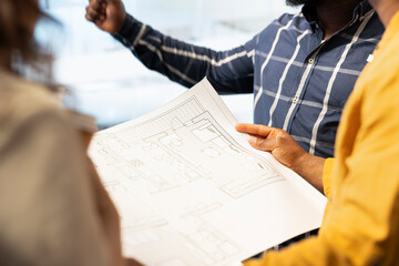 Business team evaluating architectural blueprints layout for high class office space, considering a property investment deal. Professionals negotiating with the realtor for rental agreement. Close up.