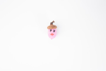 a single acorn with a painted face on white background. top view, cap is natural brown, while the body is painted pink