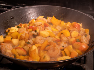 Shrimp, apples, and yellow peppers seasoned with curry powder sizzle in an iron pan with steam from the heat, creating a delicious and colorful dish.