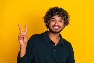 Cheerful young man making a peace sign against a vibrant yellow backdrop, expressing happiness and positivity