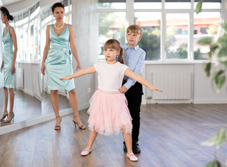 Boy paired up with girl during ballroom dancing lesson. Children rehearse waltz while female...