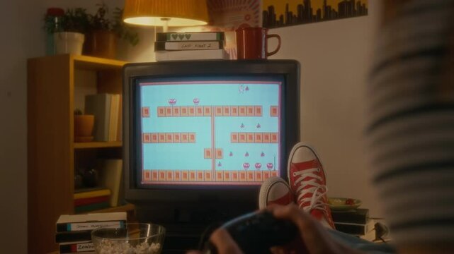 Back view of unrecognizable millennial girl playing arcade platform video game on tube TV using retro console at home, carefree and nostalgic 1990s