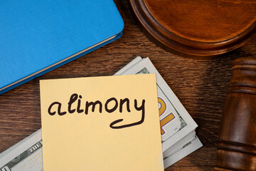 Card with word Alimony, dollar banknotes, gavel and notebook on wooden table, top view