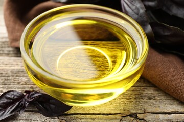 Cooking oil in bowl and red basil on wooden table, closeup