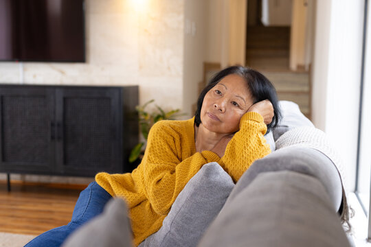 asian senior woman relaxing on couch at home, reflecting during quiet afternoon