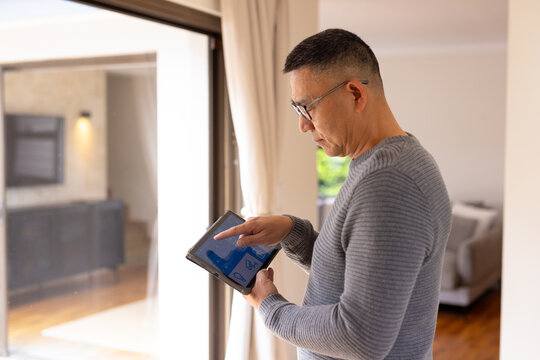 Asian senior man using tablet to control smart home system by window