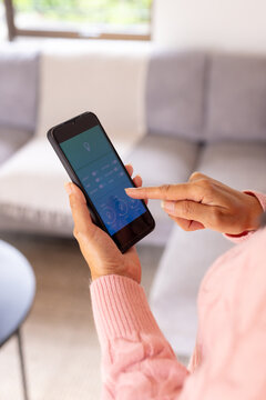 Seniro woman using smartphone app to control smart home lighting in living room
