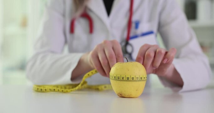 Doctor measures yellow apple with tape measure presenting weight loss concept. Specialist reminds importance of healthy eating and choices