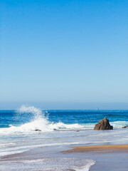 Sandy beach with waves and rocks under a clear blue sky