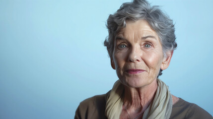 Obraz premium Portrait of elderly woman on blue. Grey-haired pensioner looks at camera. Face of elderly woman with wrinkles on skin.