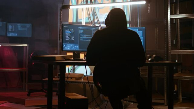 Hacker arrives in messy base of operations with neon lights and graffiti drawings sprayed on walls. Cybercriminal using ghetto hideout as HQ to commit illegal activities using computer, camera A