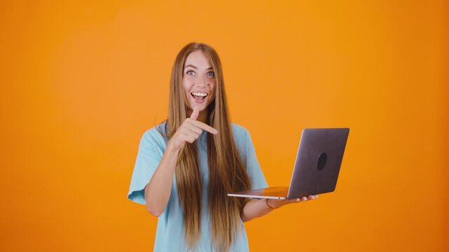 Holding her laptop, the girl types away with determination. She then turns to the camera, smiling and giving a thumbs-up, showcasing her accomplishment in the lively orange setting