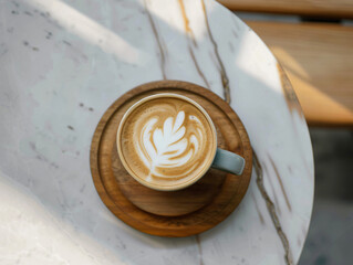 A top view of a latte art coffee presented in a light blue cup on a wooden coaster, resting on a marble table that showcases the intricate leaf design for drinks.