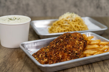 Table feast with choices of garlic noodles, clam chowder, or a fillet of tilapia and french fries on a tray to eat for dinner