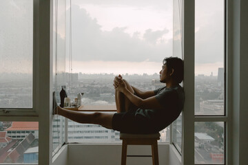 Introvert lonely asian man sitting at the windows enjoy being alone in apartment.