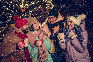 Portrait of group four buddies hold hot chocolate mug speak communicate enjoy festive atmosphere tree garland town center outdoors