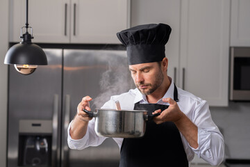 modern chef in professional uniform. close-up on the hand of male chef who is stirring soup in pot with spoon. cooking, culinary and people concept - male chef in toque with pot or saucepan.